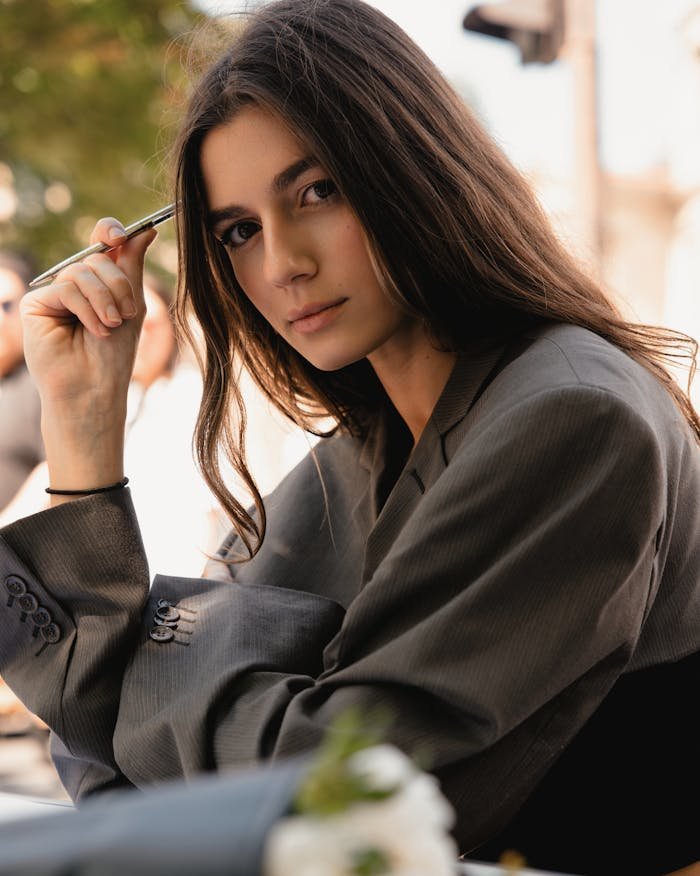 gallery-1 Confident young woman in business attire holding pen, outdoors setting.