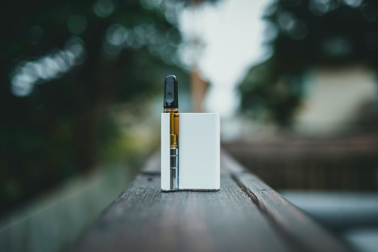 about-01 A sleek vape device resting on a wooden surface outdoors in natural light.