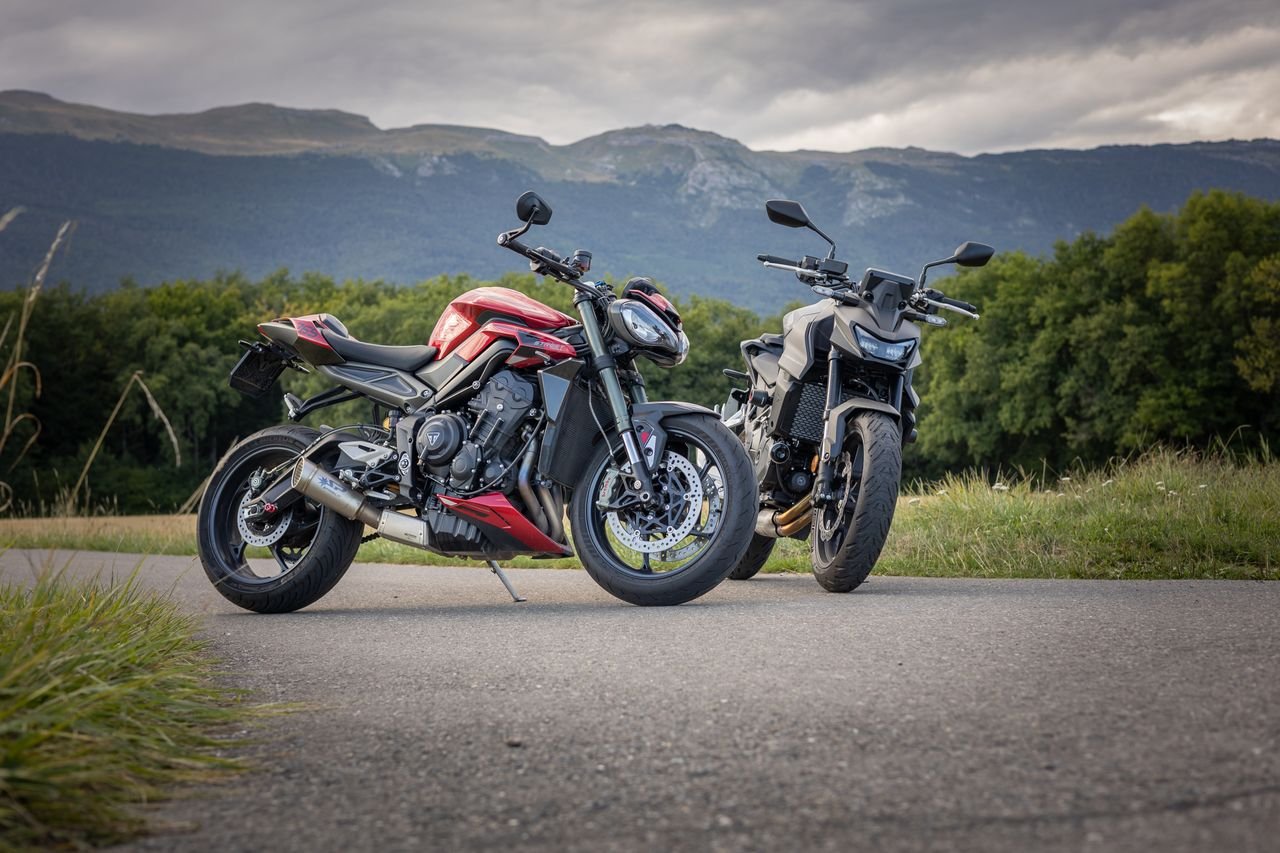 Two motorcycles parked on a rural road in Geneva, Switzerland with a scenic mountain backdrop.